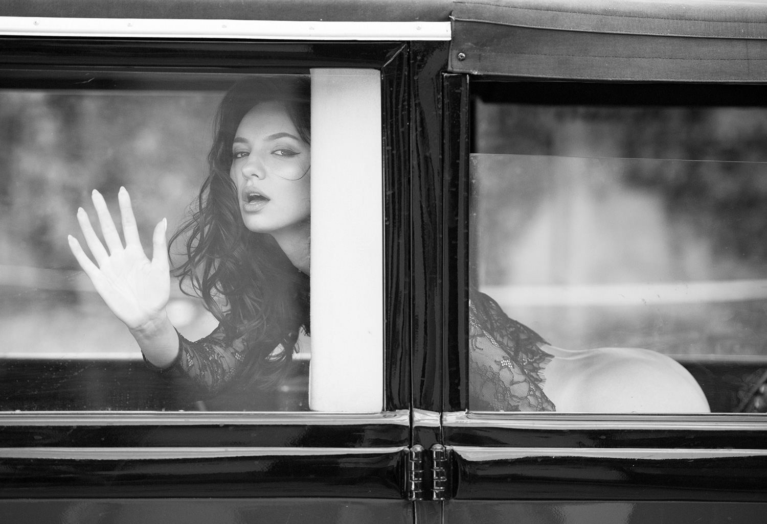 Eine Frau blickt aus dem Fenster eines klassischen Autos, ihre sinnliche Pose und der verträumte Ausdruck machen die Szene besonders