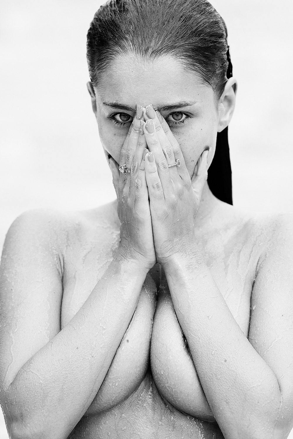Schwarz-Weiß-Porträt einer Frau mit nassem Haar, die ihr Gesicht teilweise verdeckt – künstlerische Aktfotografie.