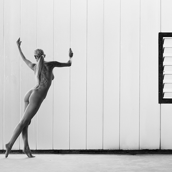 Erotic photograph of a model standing in a clear and self-confident pose in front of a pane of frosted glass and looking into the camera.