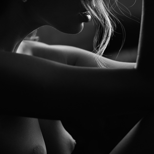 Erotic photograph of a naked woman in shadow, her silhouette emphasized by soft light, in a moment of intimacy and contemplation.