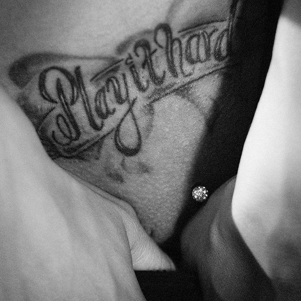 Erotische Aktfotografie mit Tattoo „Play it Hard“, Nahaufnahme mit Piercing, Schwarz-Weiß.