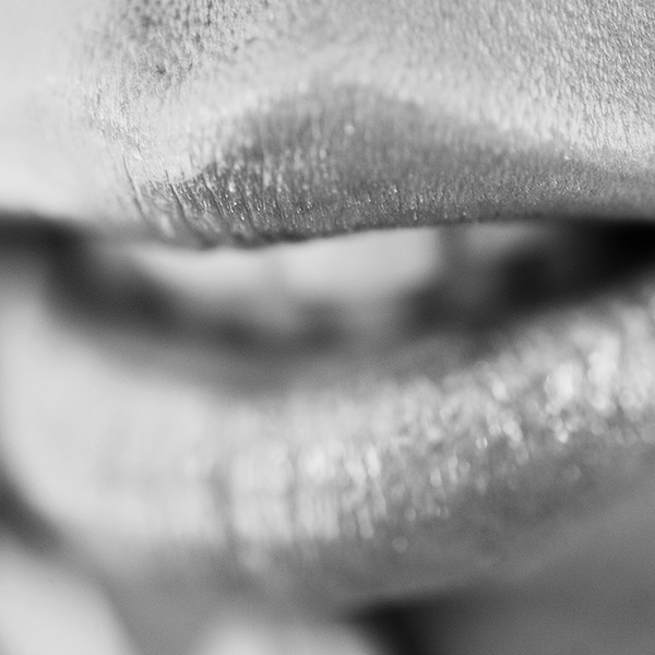 Erotic photograph of a close-up of lips depicted in soft light and shadow, creating a subtle, seductive atmosphere.