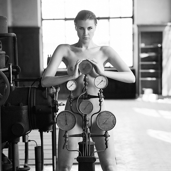 Erotic photograph of a naked woman standing with a powerful pose under pressure knives, embodying the tension of the moment.