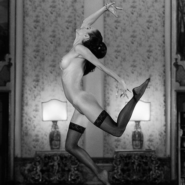 Erotic photography: A naked woman in sexy stockings dances in an elegant room and leaves gravity behind, the focus is on dynamic movement and sensual elegance.